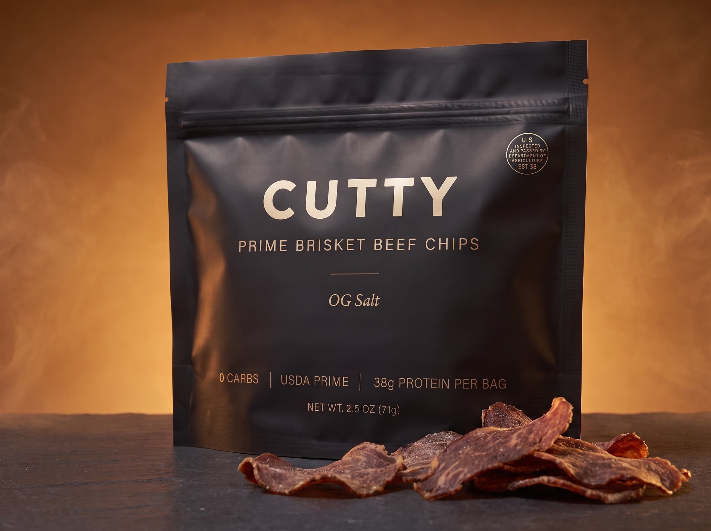 CUTTY pouch shot at a low angle with brisket chips scattered in the foreground under warm light