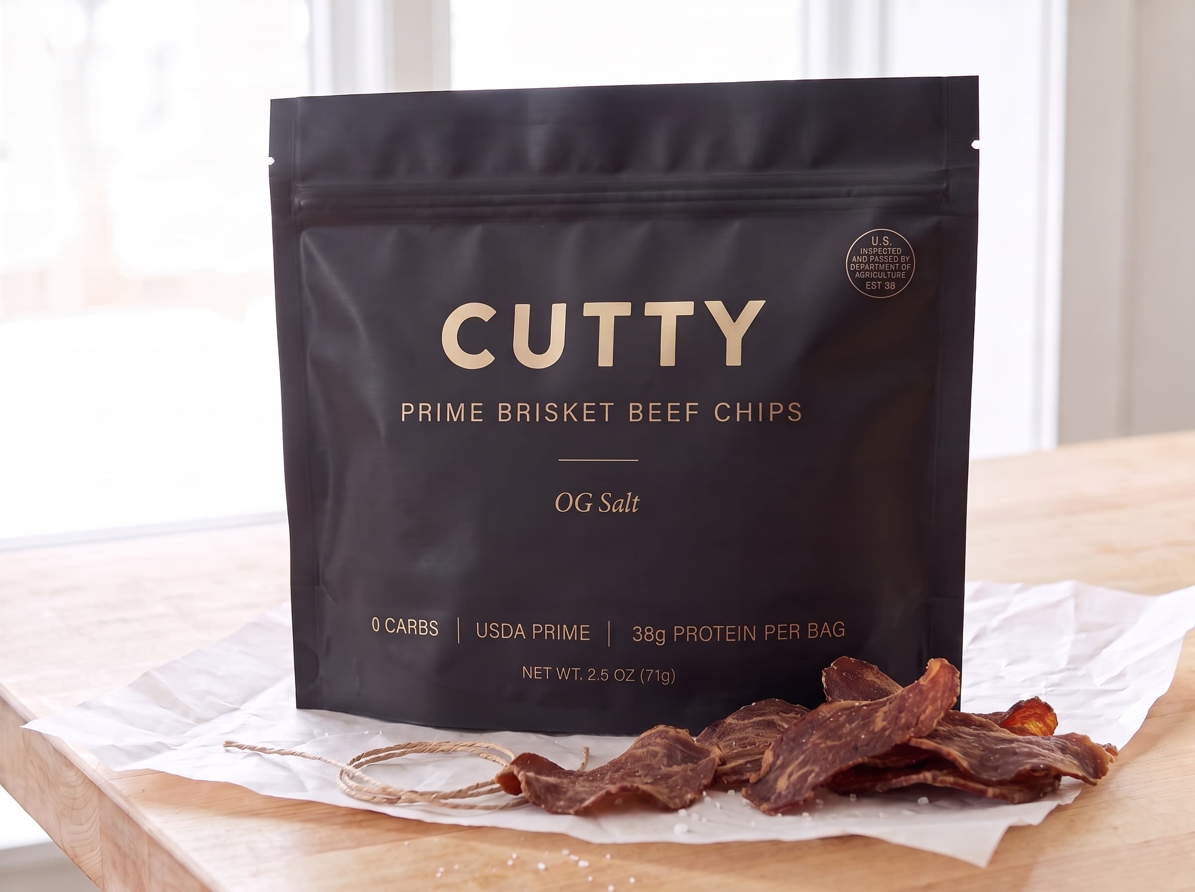 Black CUTTY pouch resting on bone-white butcher paper in soft daylight, brisket chips and twine beside it
